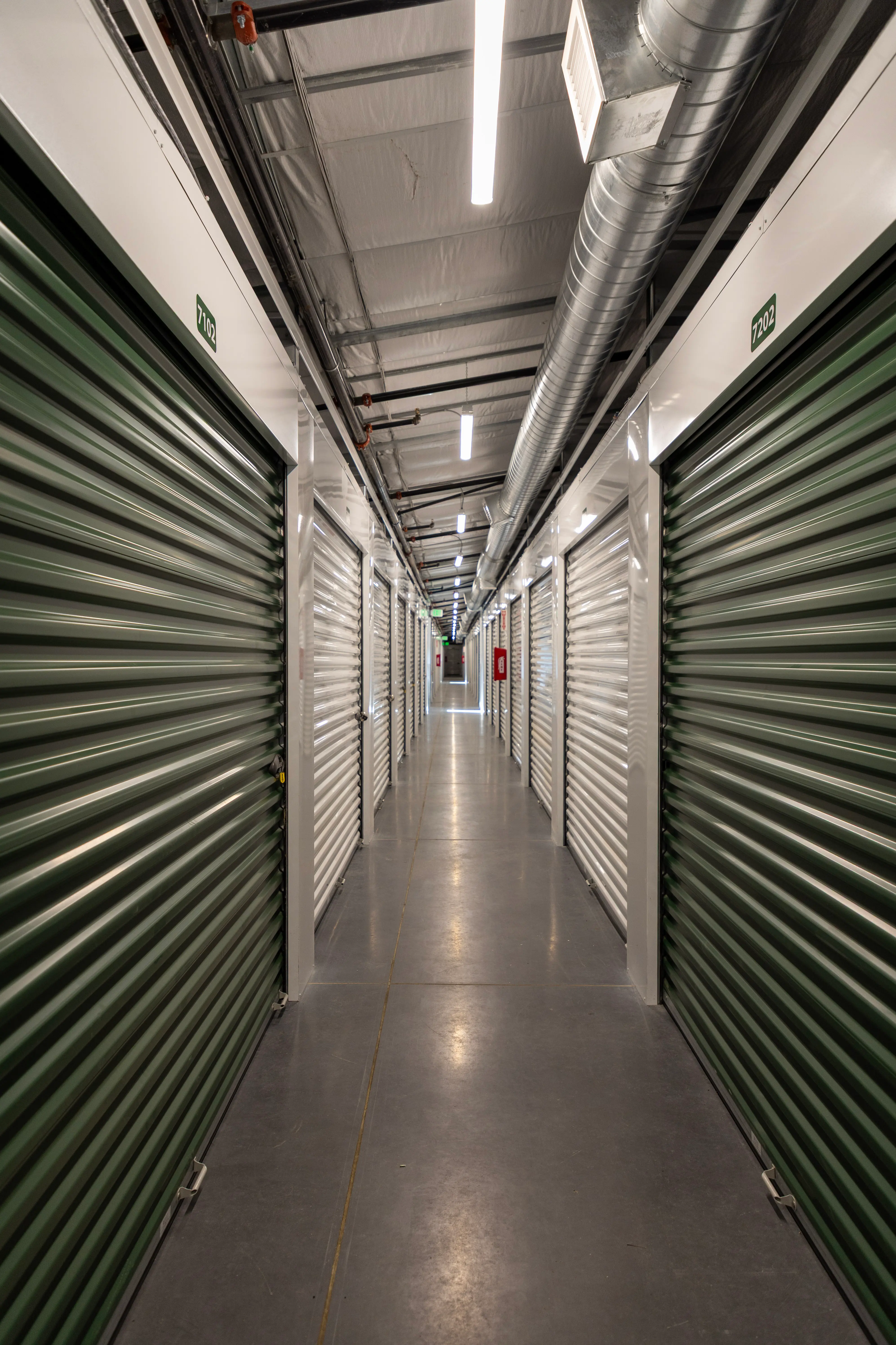 Long interior hallway lined with green roll-up doors in the climate-controlled building