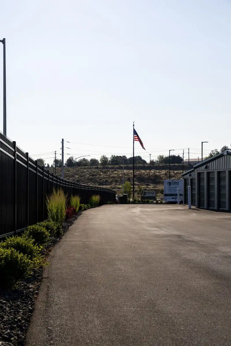 Drive aisle between perimeter fence and storage buildings, American flag in the distance
