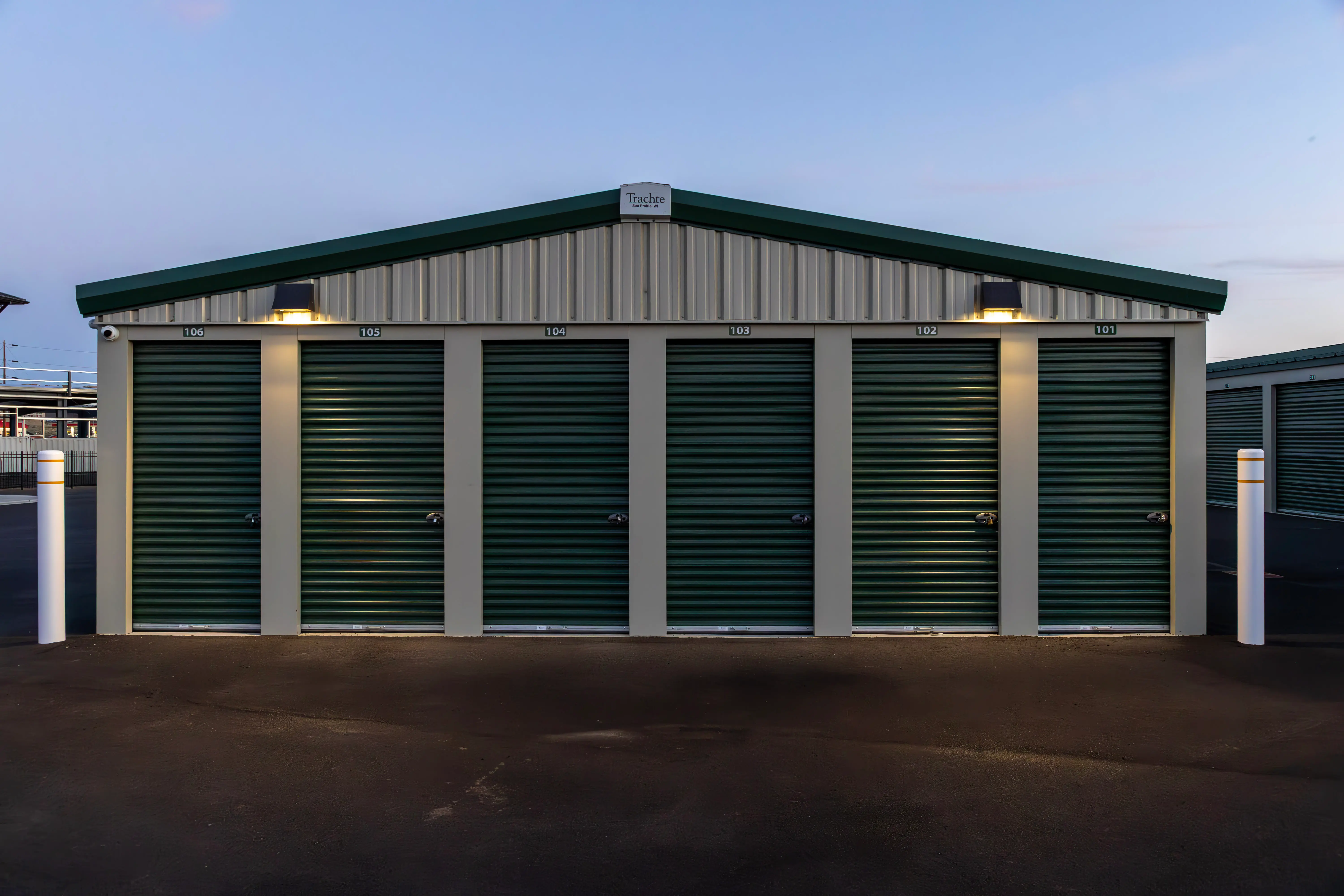 Symmetric front view of a row of drive-up units with green roll-up doors at dusk