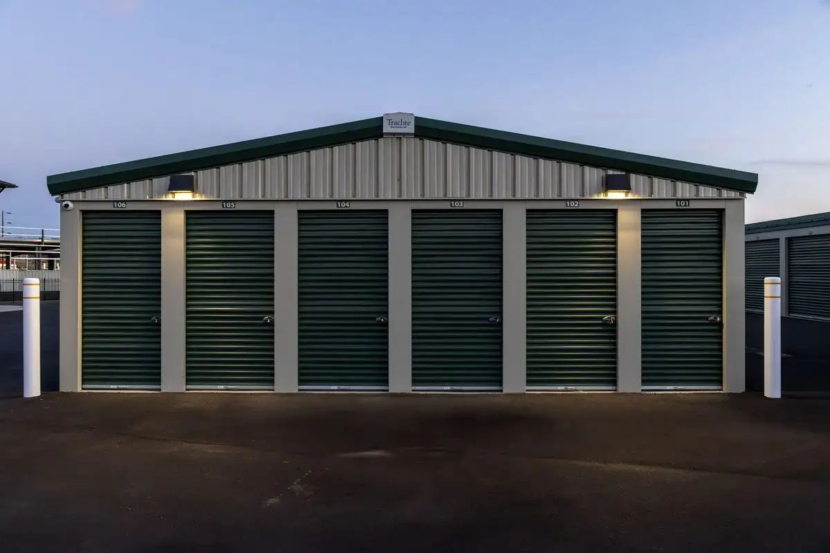 Symmetric front view of a row of drive-up units with green roll-up doors at dusk